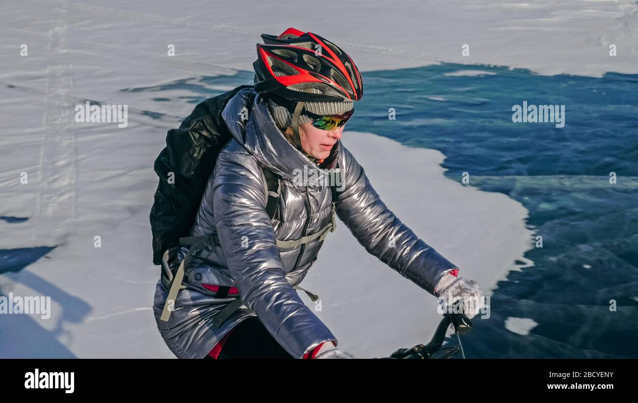 Woman is riding bicycle on the ice. Tires on bike are covered wi Stock