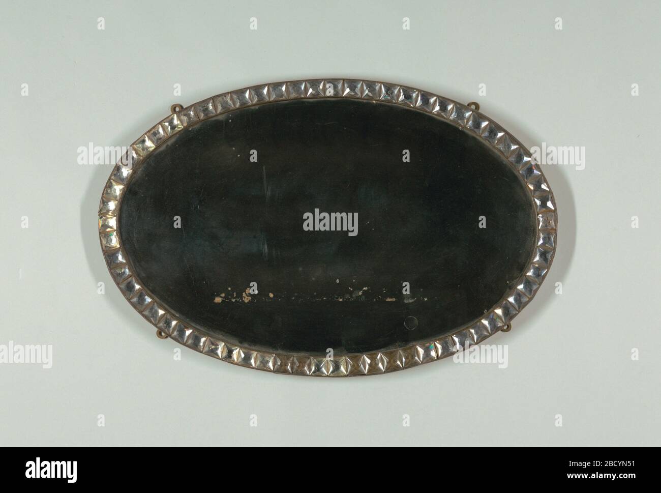 Mirror. Research in ProgressOval mirror surrounded by oval metal frame with row of square, faceted glass 'jewels'; wood backing; four mounting rings on reverse, allowing vertical or horizontal orientation. Mirror Stock Photo