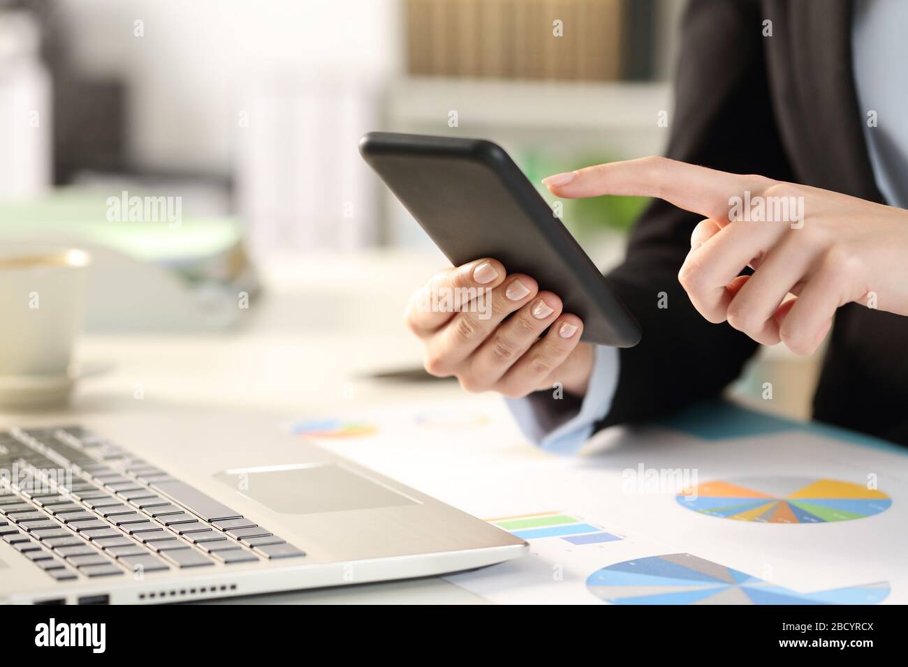 Close up of business woman hands checking smart phone on a desk at the office Stock Photo