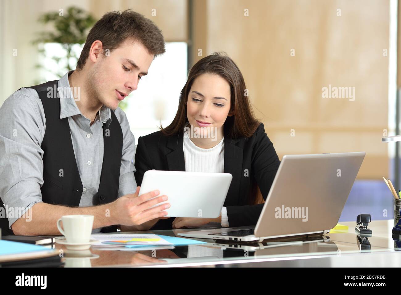 Man employee helping coworker girl showing tablet sitting at office desk Stock Photo