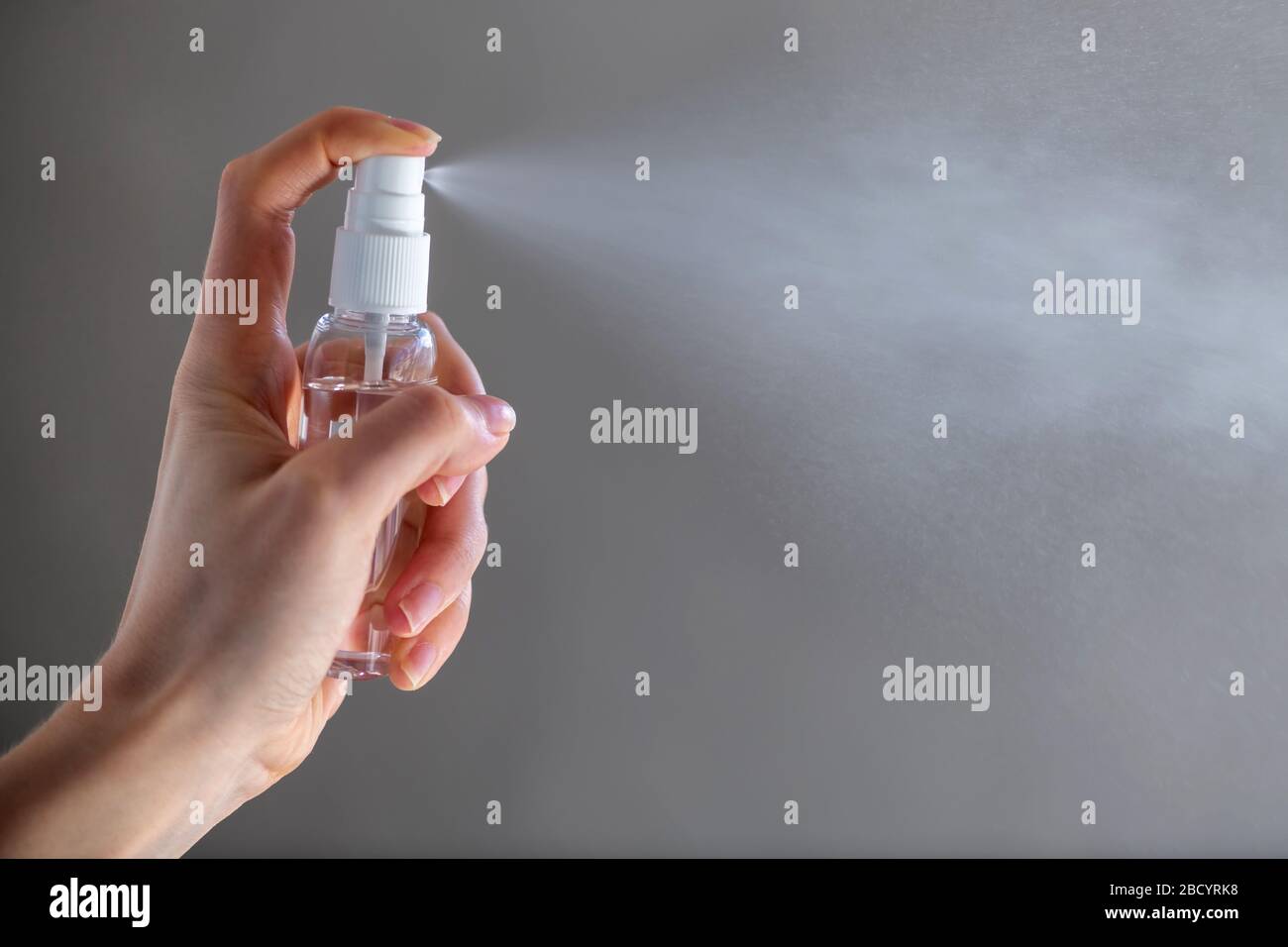 Female person woman or girl applying spray disinfectant alcohol product on hand disinfecting hands against virus bacteria health prevention on gray ba Stock Photo