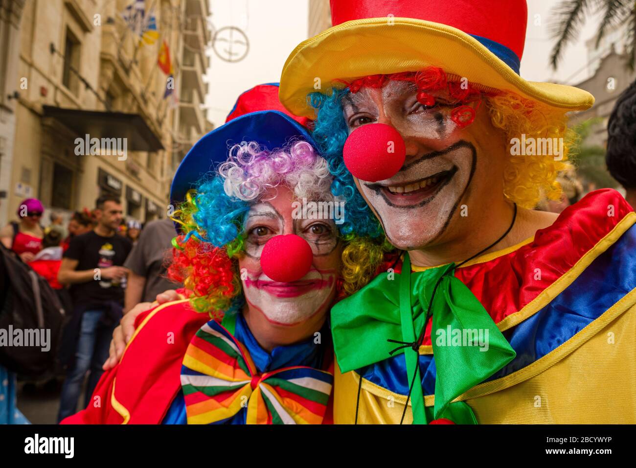 A man and a woman, dressed up as clowns and smiling, partying in the streets during the Daytime Carnival Stock Photo