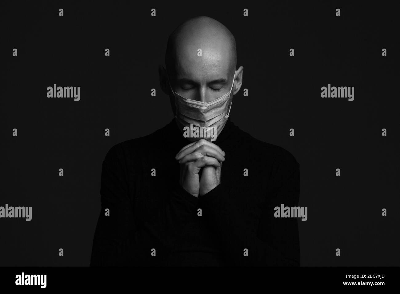 Coronavirus, Bio Protection Concept. Close up portrait of handsome bald man wearing medical mask, black turtleneck and praying. Copy-space. Studio sho Stock Photo