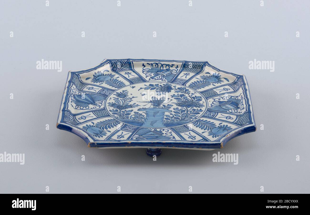 Tray. Research in ProgressFlat 8-sided tray with raised rim, on three flattened ball feet; painted in underglaze blue on white with center roundel showing dragonfly, rocks, flowers, surrounded by 8 panels painted with 'precious objects' alternating with flowers; feet painted blue. Tray Stock Photo