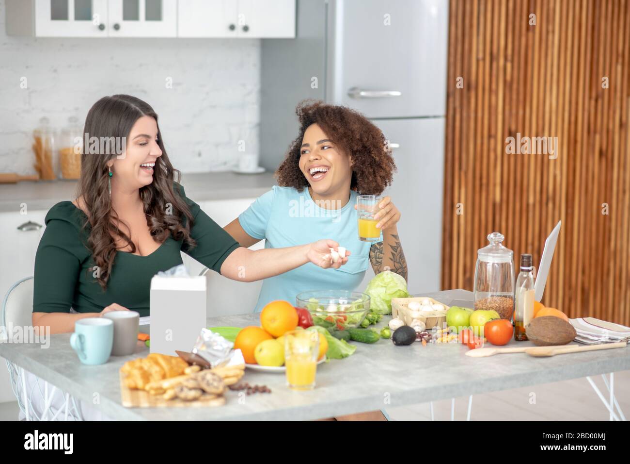 Two young women happily chatting at the kitchen table. Stock Photo