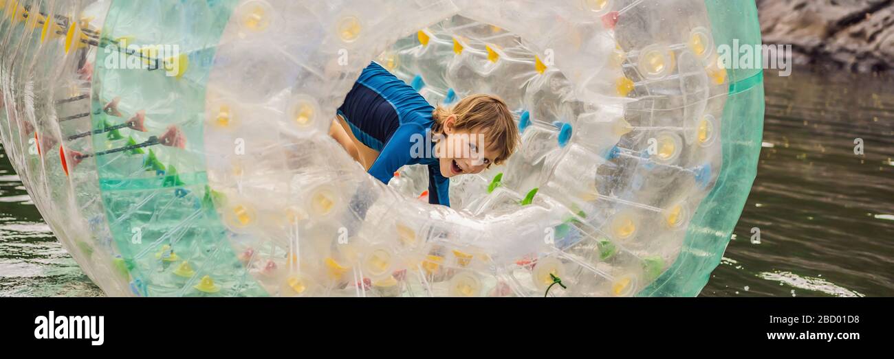Cute little boy, playing in Zorb a rolling plastic cylinder ring with a hole in the middle on the lake BANNER, LONG FORMAT Stock Photo