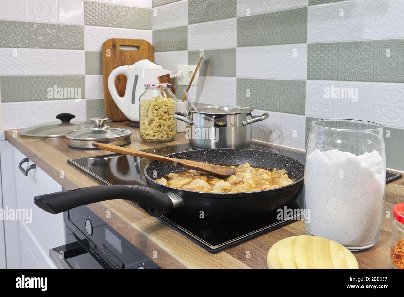 The meat is fried in pan on hob. Kitchen interior, cooking utensils