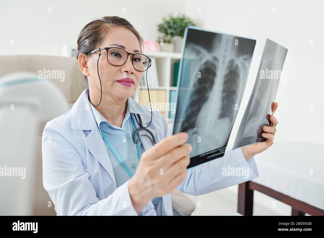 Serious mature Vietnamese woman examining chest xrays of patient with
