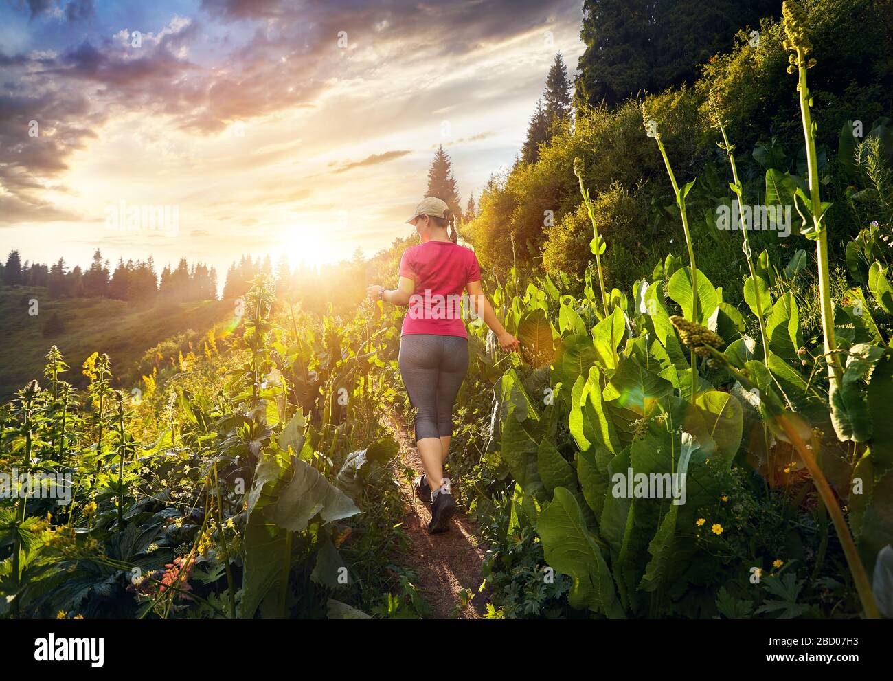 Beautiful sporty girl in pink shirt walking in the mountain trail at cloudy sunset sky Stock Photo