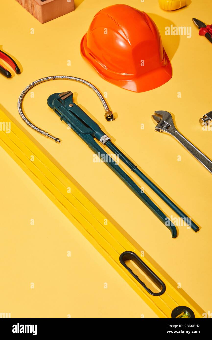 high angle view of calipers, helmet, monkey wrench, spirit level, brick,  pliers and plumbing hose on yellow background Stock Photo - Alamy