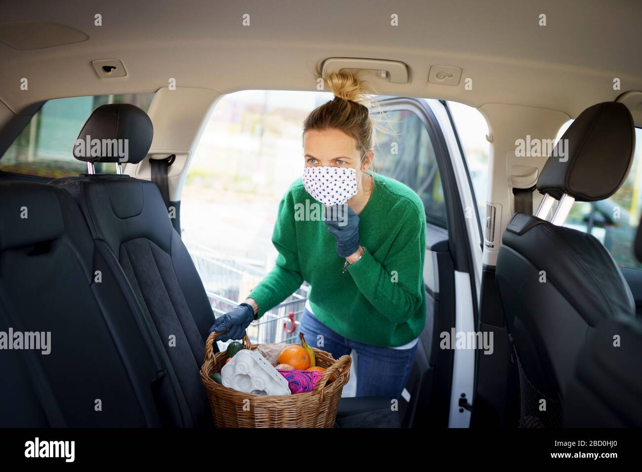 beautiful young woman is shopping with mouth protecting mask during corona covid crisis and is holding her shopping basket Stock Photo