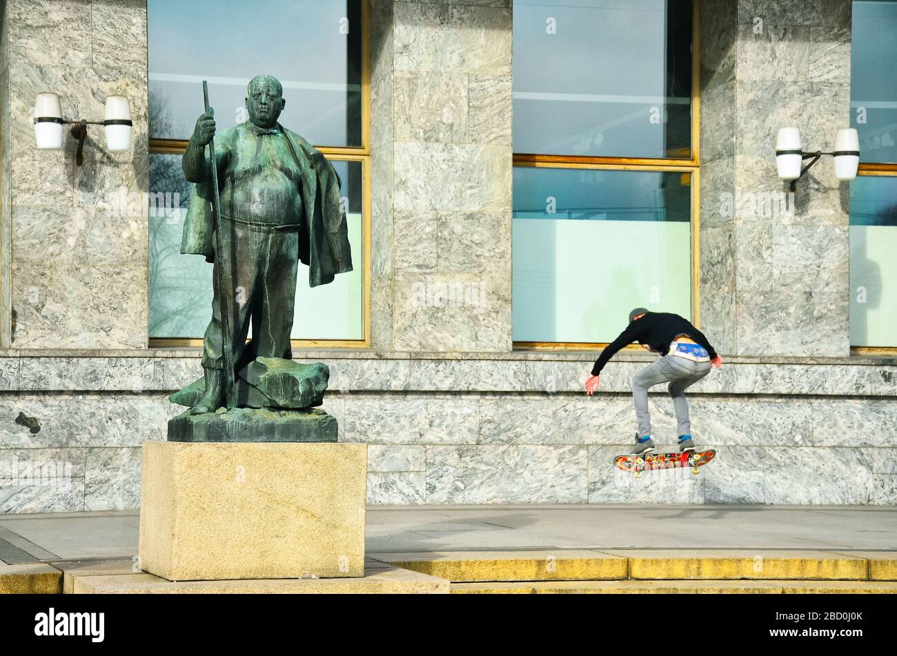 Young man jumping on skateboard in oslo near by statue of fat man Stock Photo