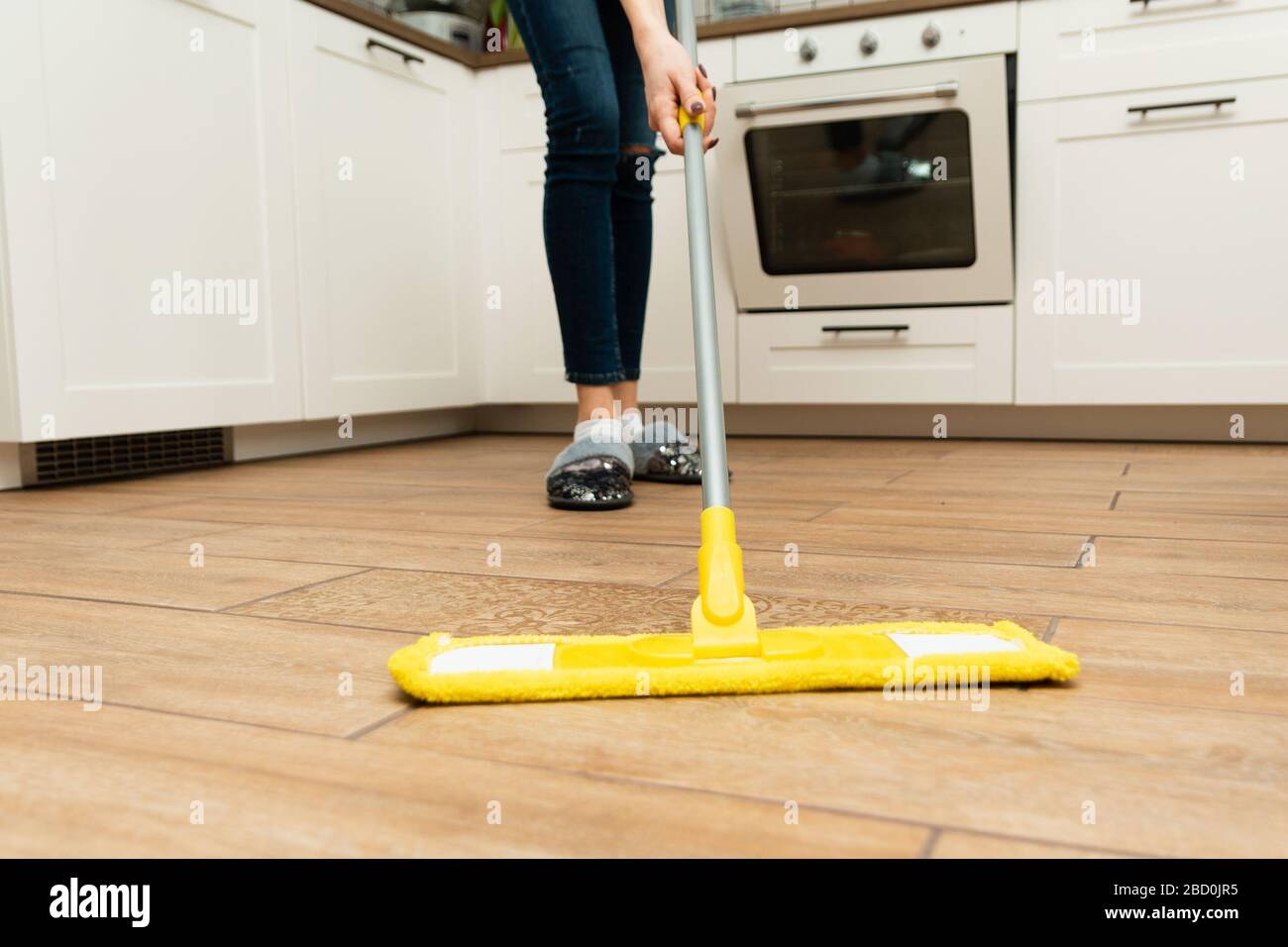 Worth housewife cleaning floor at home. Lovely woman washes wooden floors from a laminate in a bright kitchen. Stock Photo