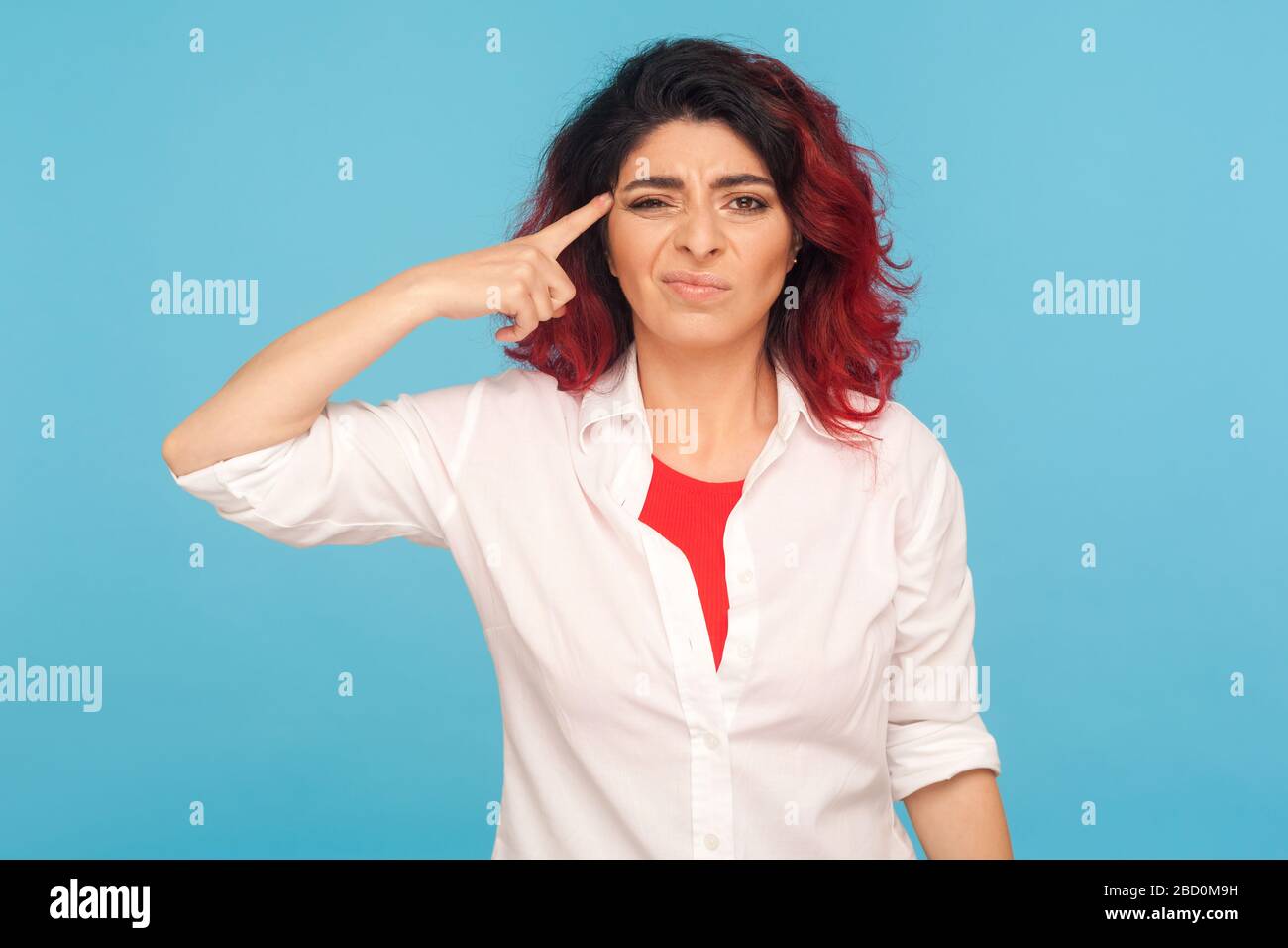 Bad idea. Portrait of disappointed unhappy woman in white shirt making stupid dumb cuckoo gesture with finger near head, dissatisfied with senseless t Stock Photo