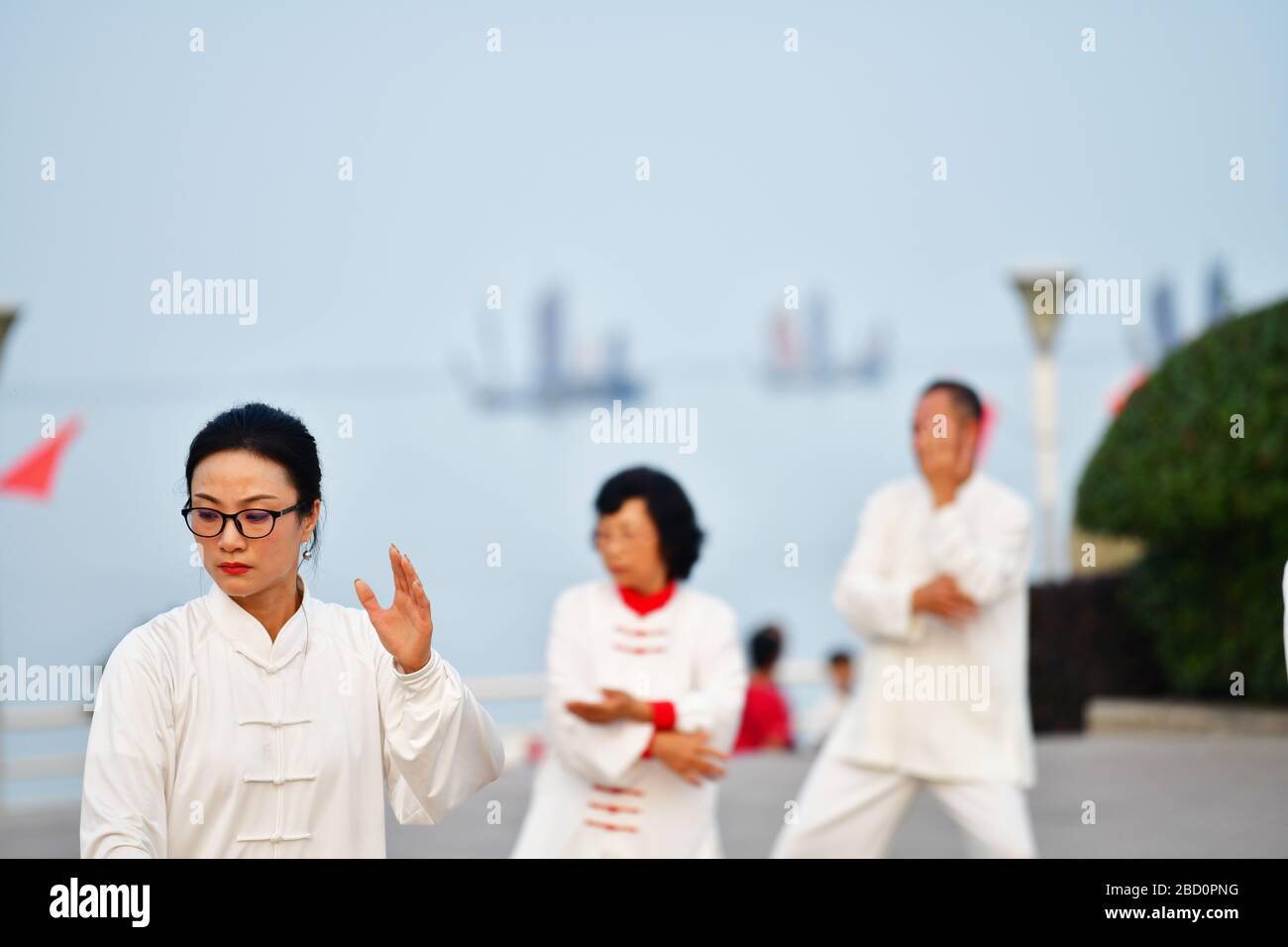 Huzhou, China, October 2019; View on woman in focus part of larger group of people  (out of focus) practicing Tai Chi, Yang style in early evening Stock Photo