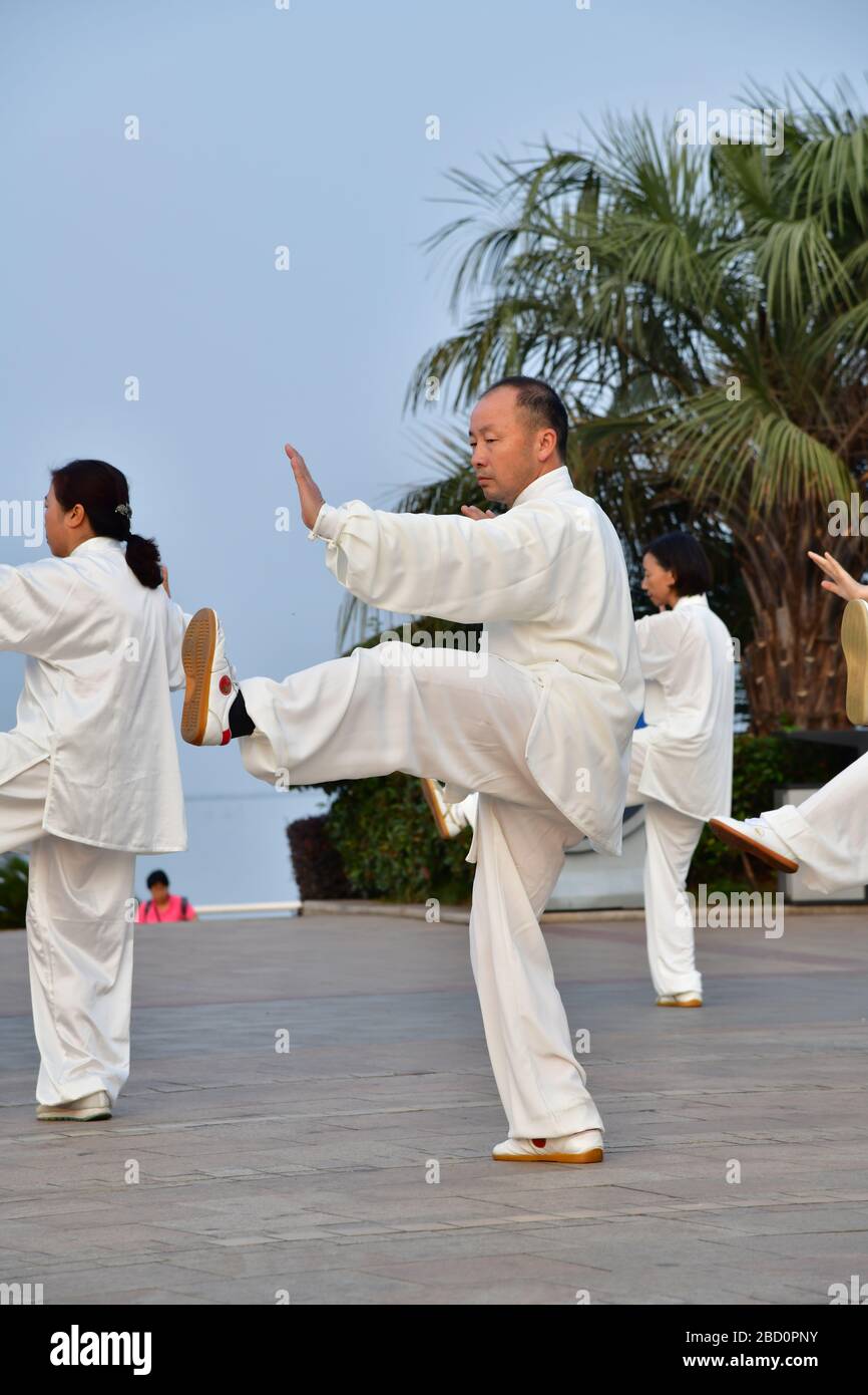 Huzhou, China, October 2019; Man practicing Tai Chi, Yang style as part of a larger group of people in early evening on the shore of Tai Lake Stock Photo