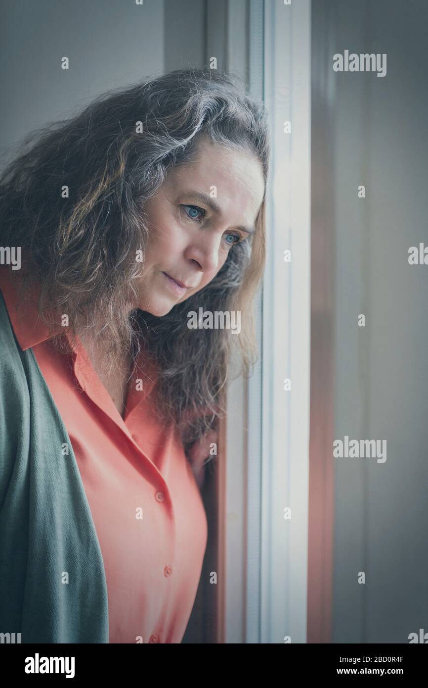 Thoughtful woman leaning her head on a window staring outside watching something intently Stock Photo