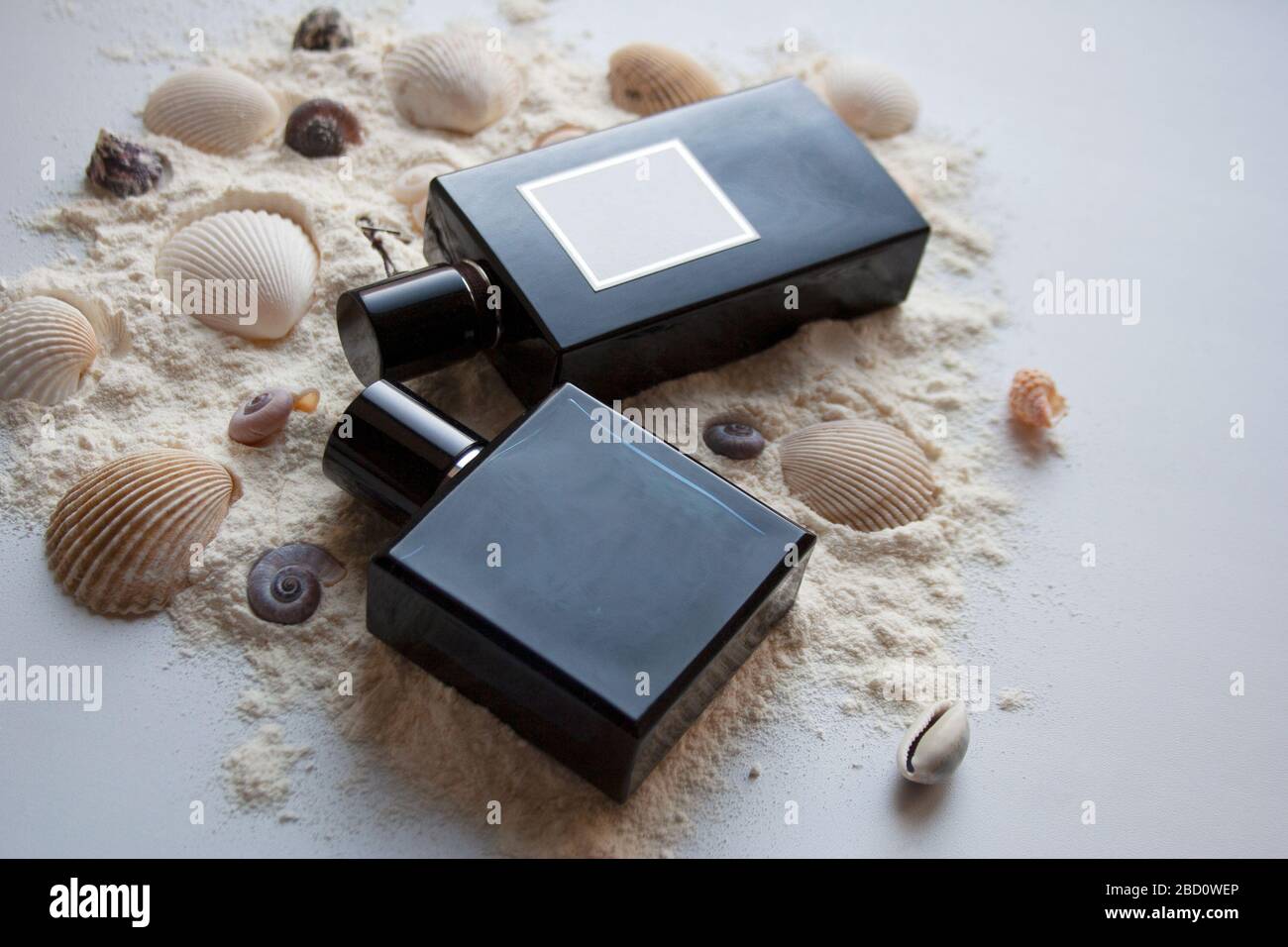 Two dark glass perfume bottles on sand with seashells Stock Photo
