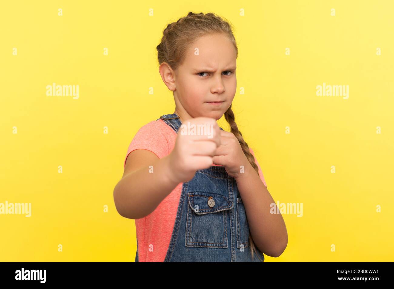 Portrait of brave fighting little girl in overalls standing with boxing