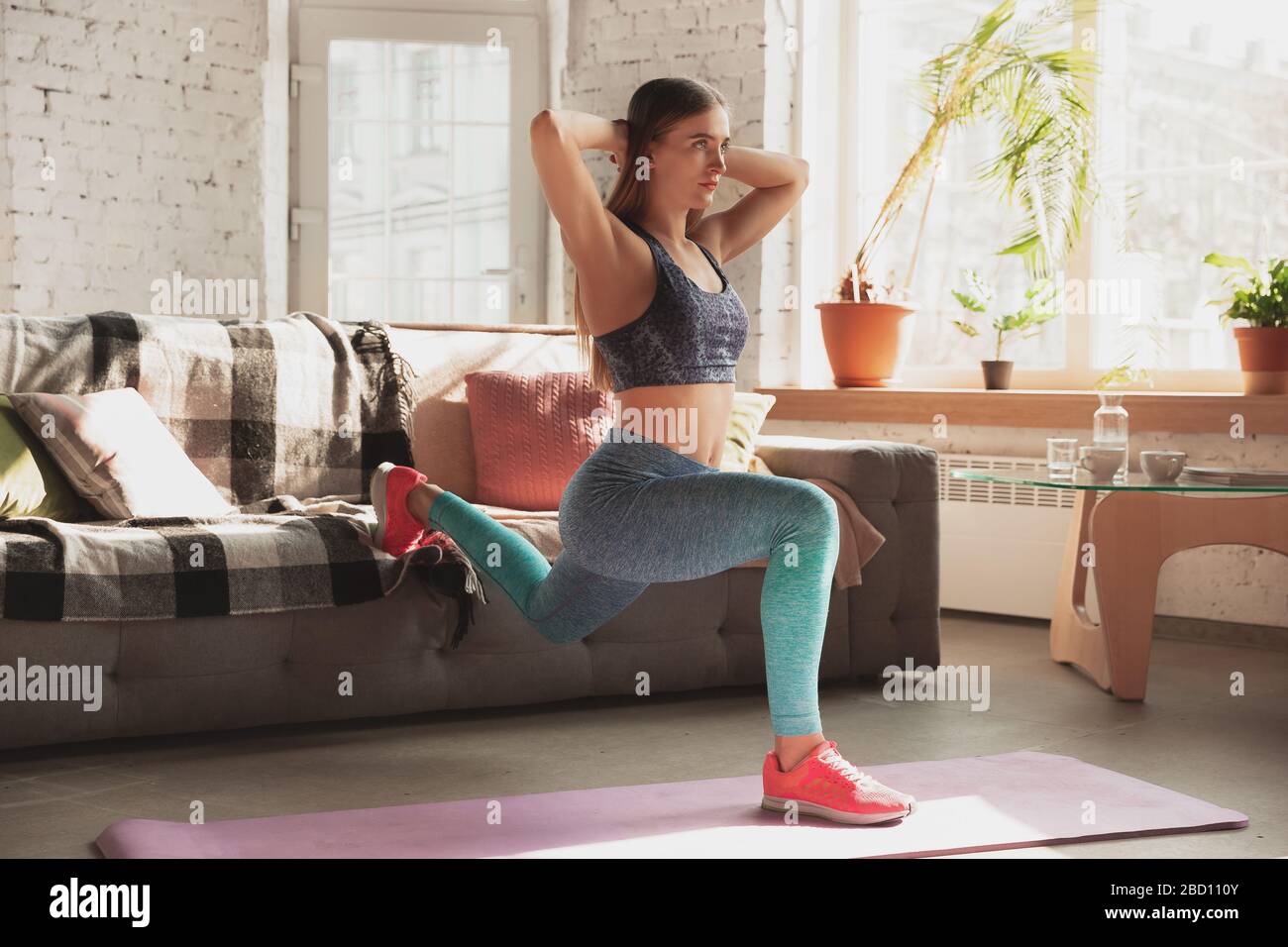 Young woman teaching at home online courses of fitness, aerobic, sporty lifestyle while quarantine. Getting active while isolated, wellness, movement concept. Exercises for stretching, balance. Stock Photo