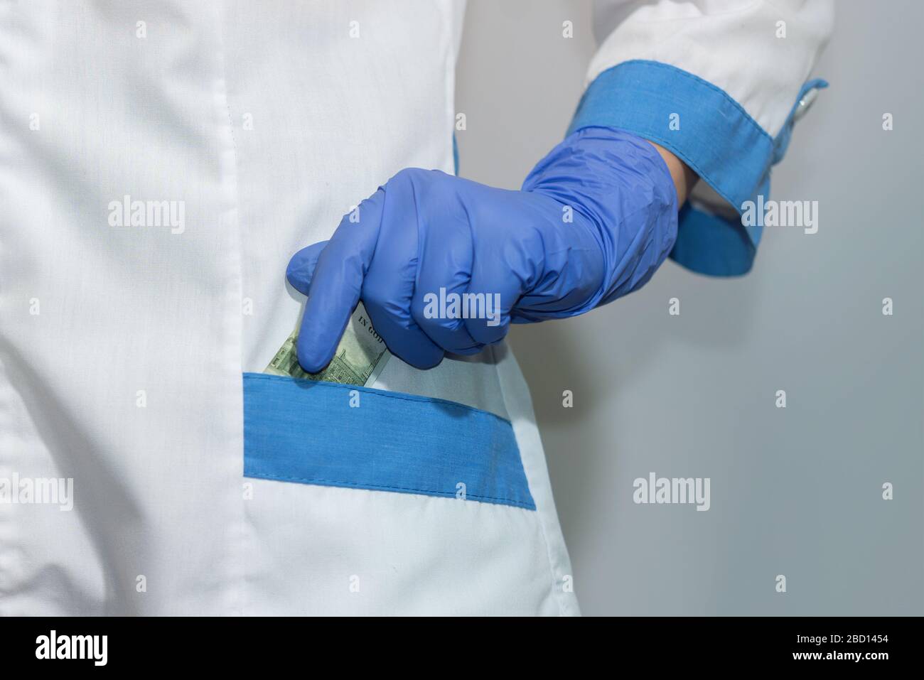 A doctor or paramedic hides a hundred dollar bill in his pocket Bribe. Corruption in medicine, pharmaceuticals. The concept of paid medicine. Stock Photo