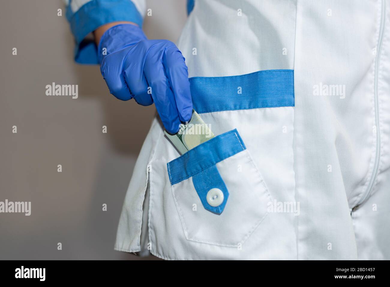 A doctor or paramedic hides a hundred dollar bill in his pocket Bribe. Corruption in medicine, pharmaceuticals. The concept of paid medicine. Stock Photo