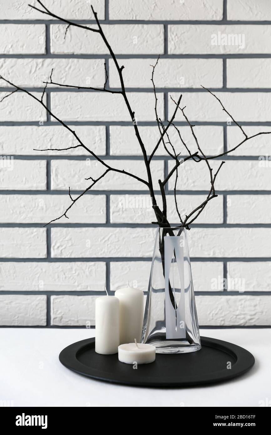 Dry tree branches in a vase on a black tray with candles against a