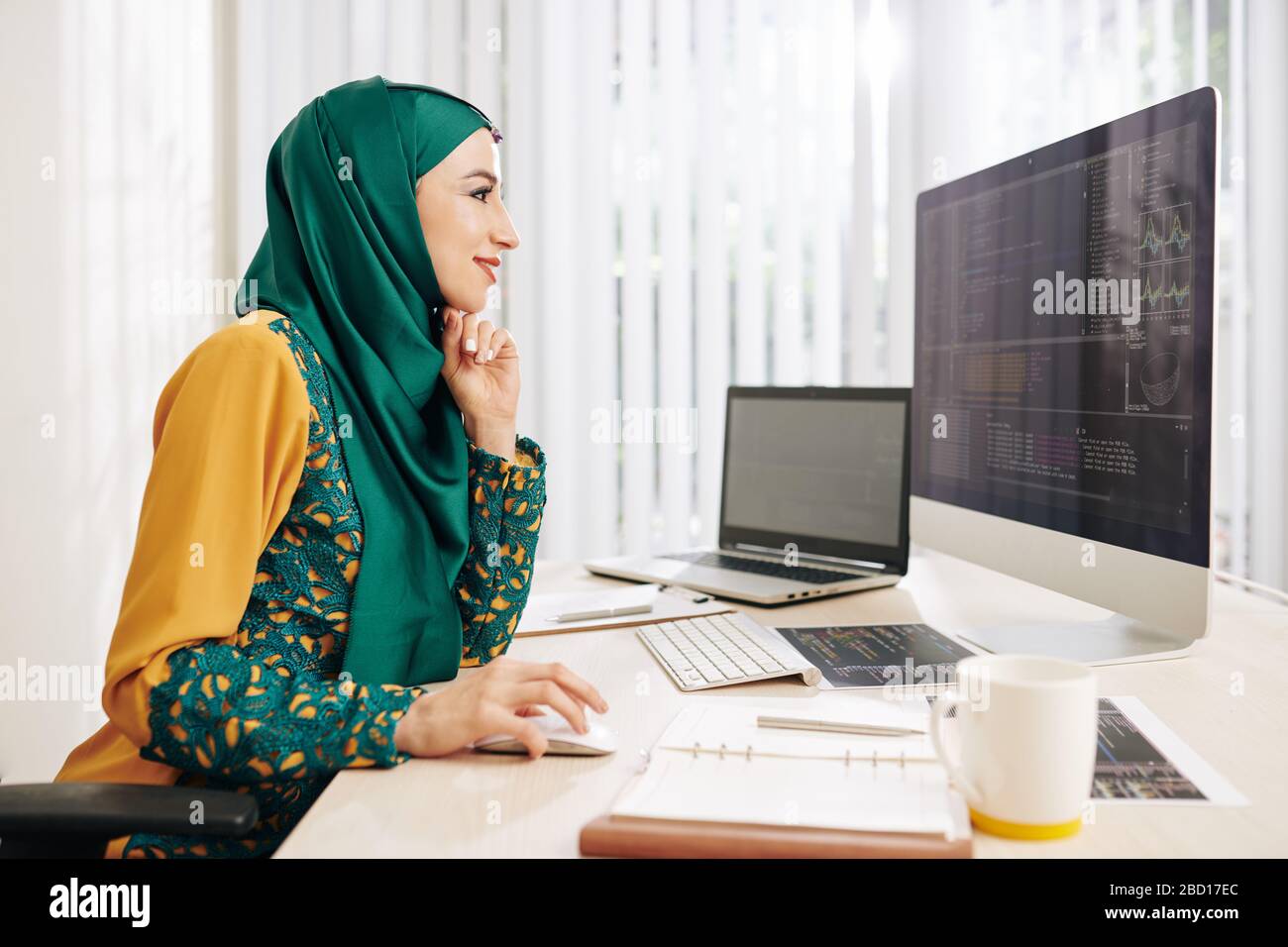 Smiling muslim young woman in traditional dress enjoying working on new ...