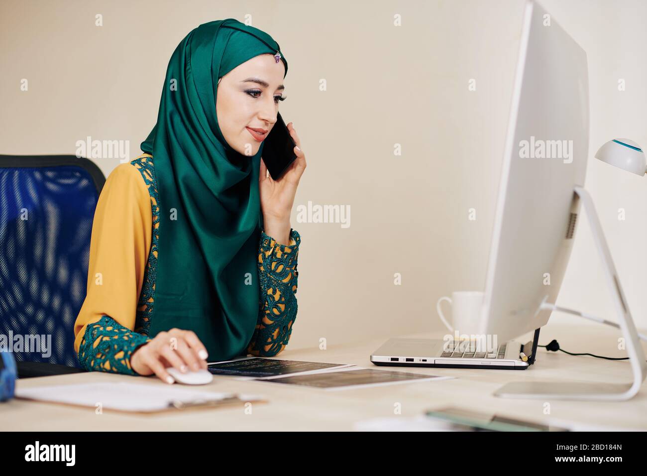 Smiling muslim female software developer talking on phone with client Stock Photo