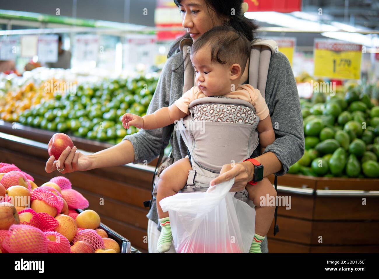 mother shopping in grocery store while carrying her baby Stock Photo