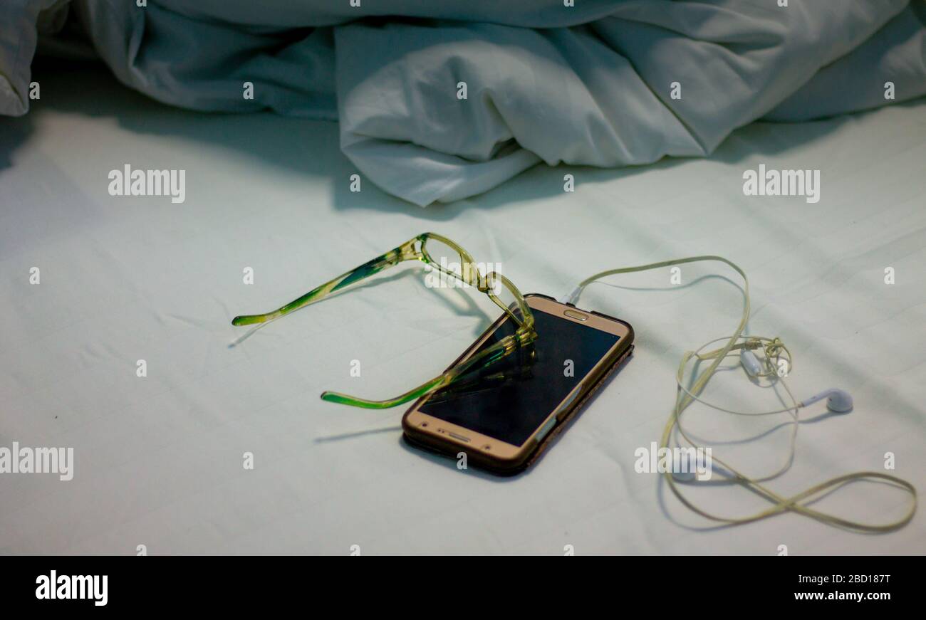 on the bed and with a blanket there are mobile phones and headphones placed, he looked messy the bed was wrinkled after waking up late that day, nobod Stock Photo