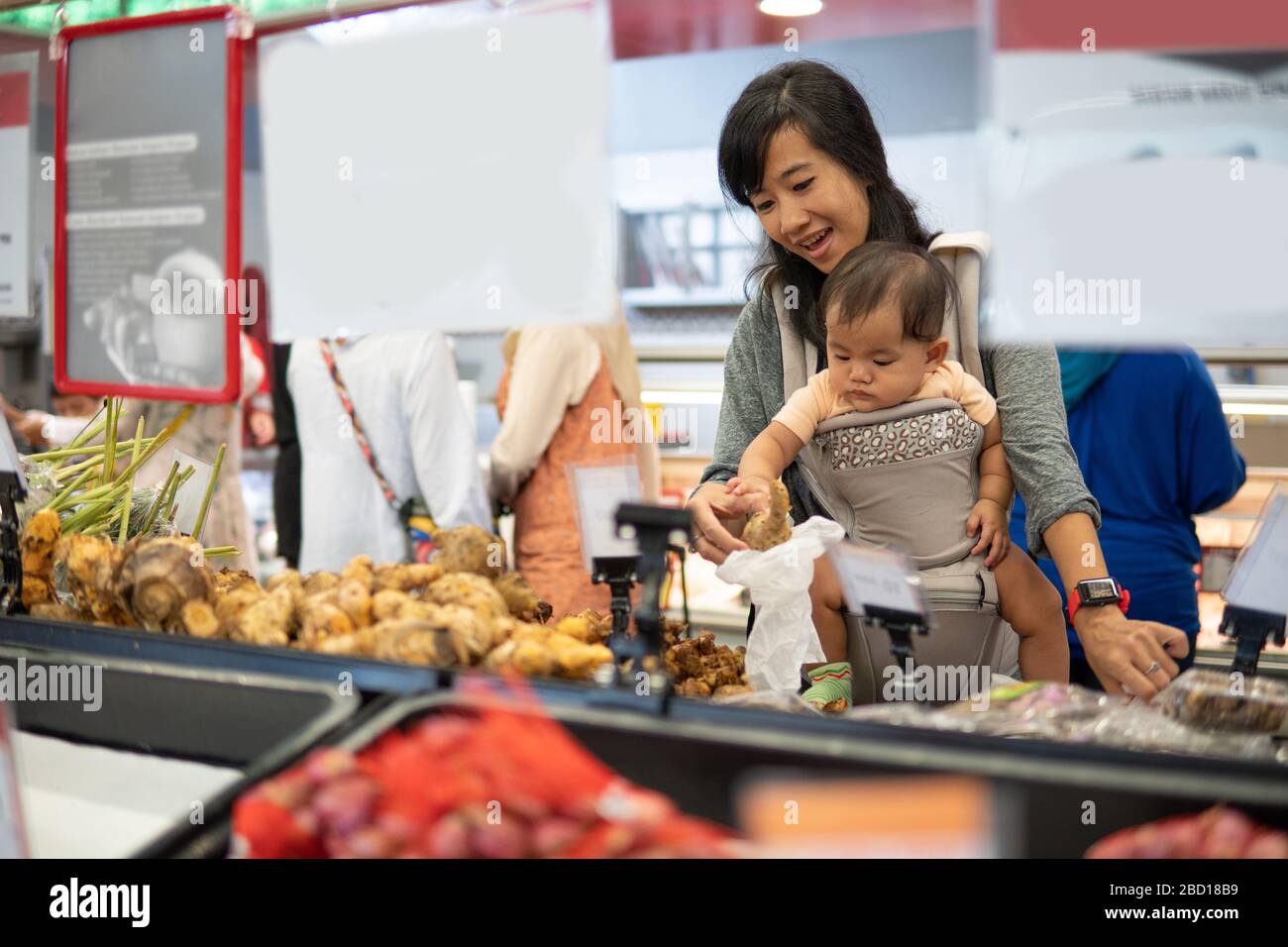 mother shopping in grocery store while carrying her baby Stock Photo