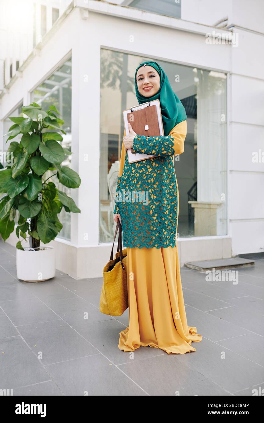 Happy smiling muslim female student with clipboard and tablet computer standing outdoors Stock Photo
