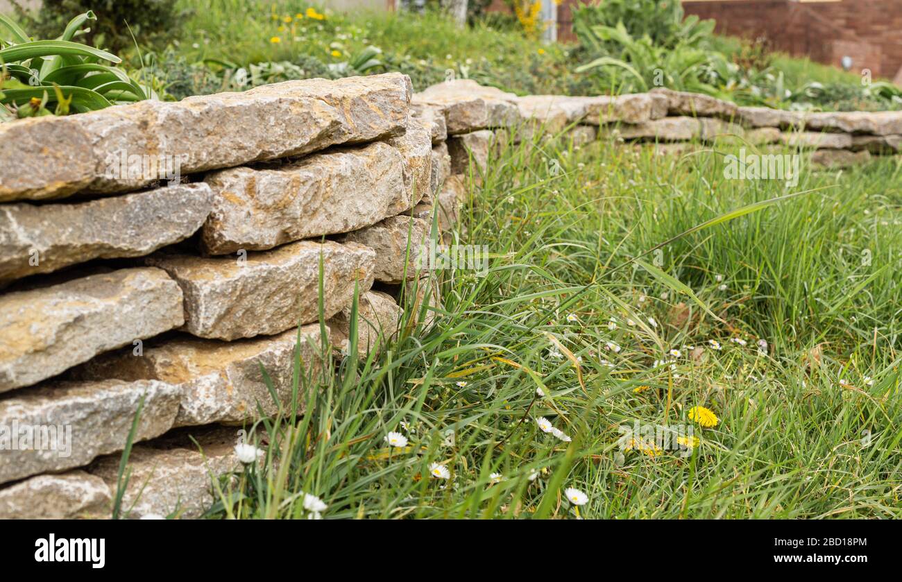 Wall made of stones in a city park. City Gardens. Fenced off from the lawn. Retaining wall. Stock Photo