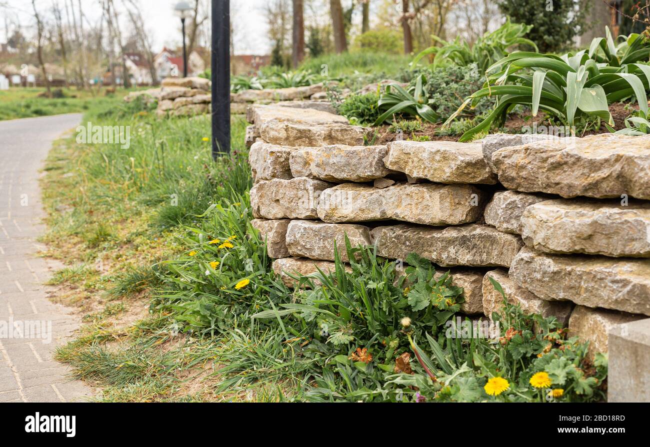 Wall made of stones in a city park. City Gardens. Fenced off from the lawn. Retaining wall. Stock Photo