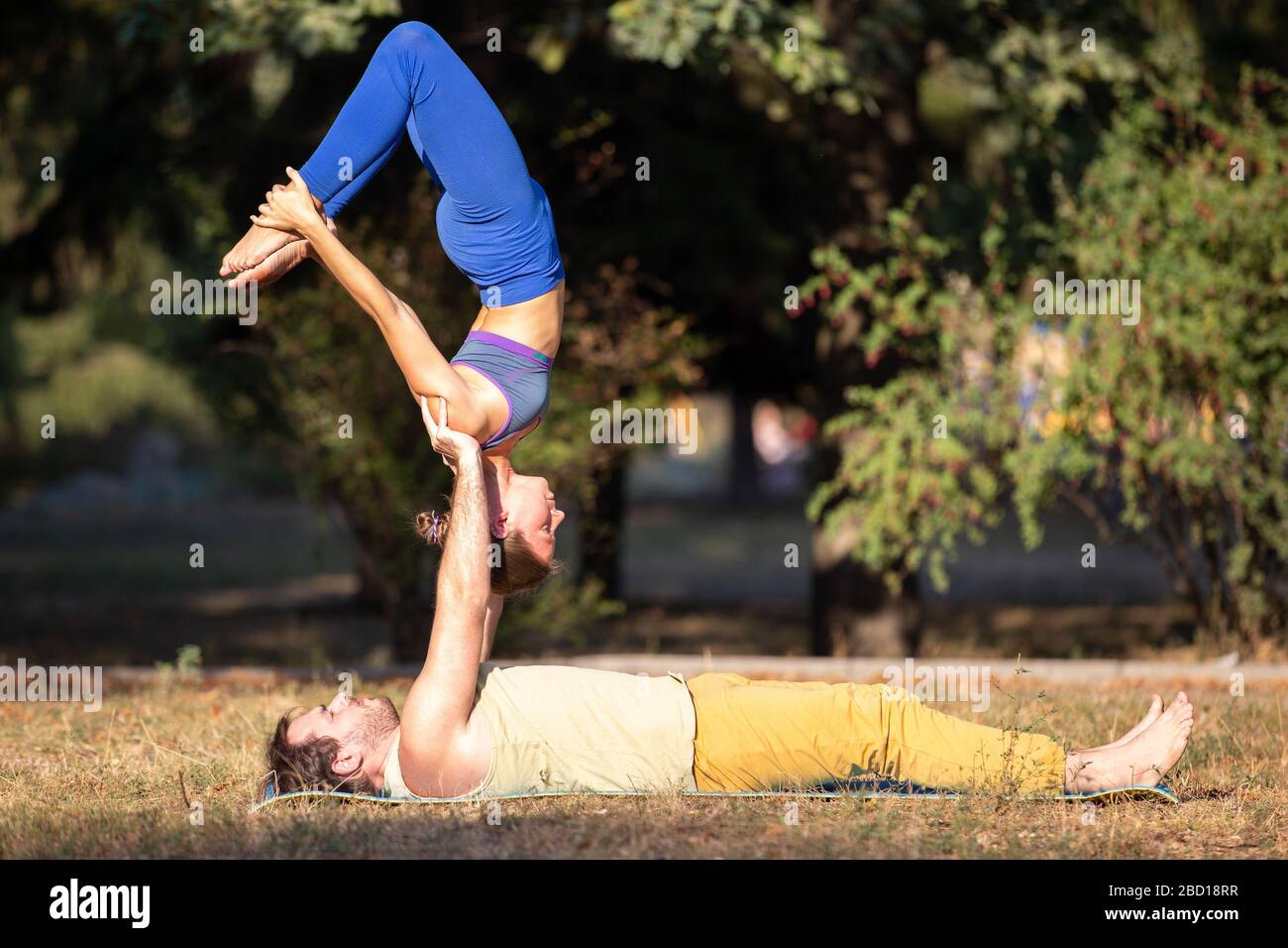 young couple doing acroyoga exercises in park man holding woman on hands in acro yoga poses 2BD18RR