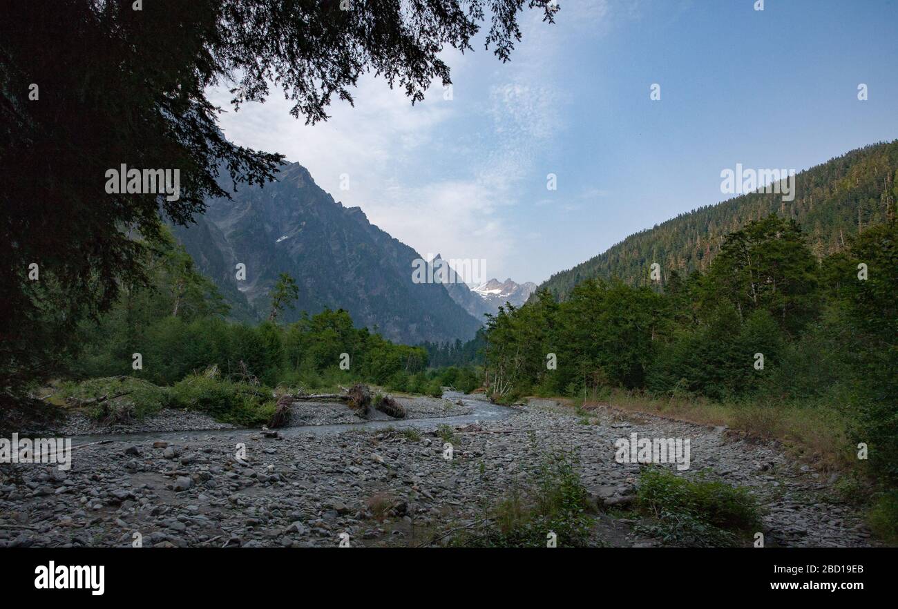 A shaded mountain stream runs through a valley between tree-covered mountainsides. Stock Photo