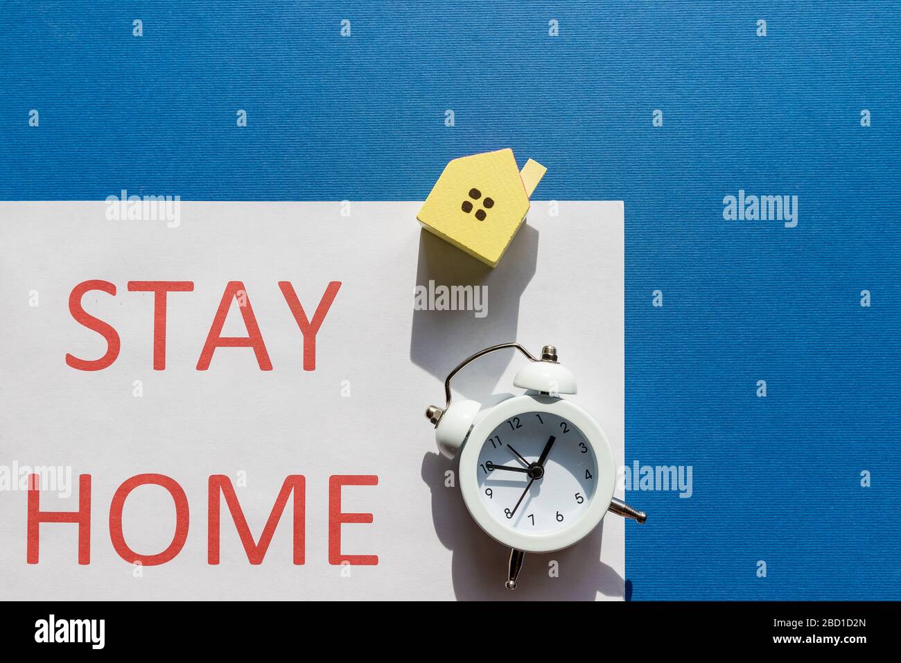 alarm clock and small house toy on a blue background, text time to stay home in quarantine during the coronavirus pandemic.self isolation concept Stock Photo