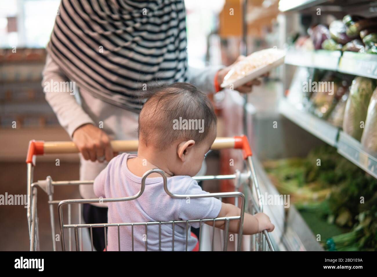 happy infant baby sitting in shopping cart or trolley in grocery