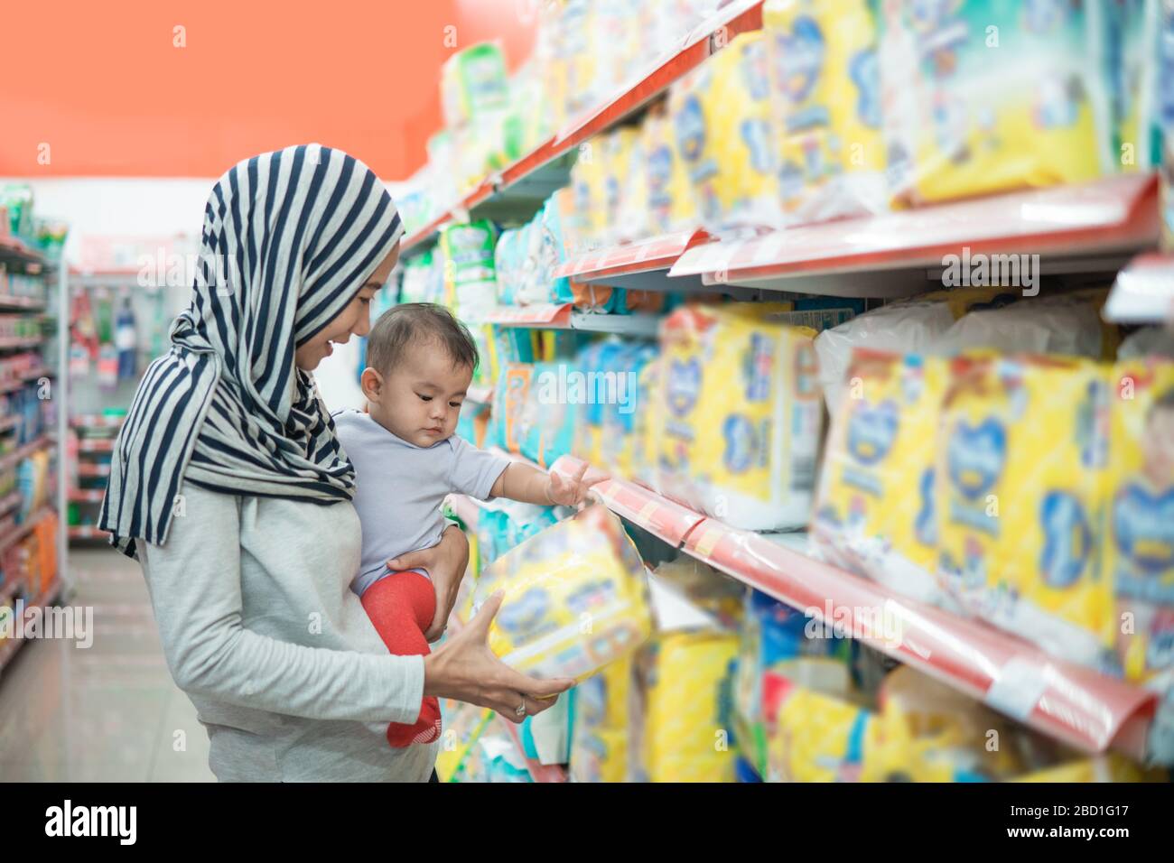 muslim asian mother buying baby product while carrying her daughter Stock Photo