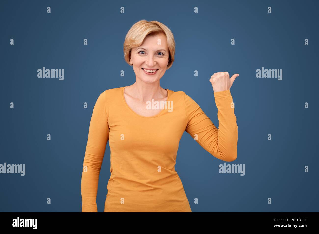 Happy mature woman pointing with thumb aside Stock Photo