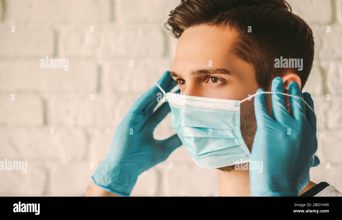 Young man in blue latex gloves putting on medical mask on face ...