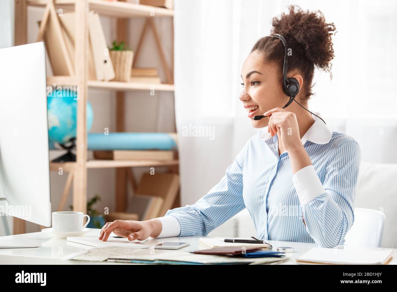Tour agent in headset sitting at table in office talking with customer browsing computer joyful Stock Photo