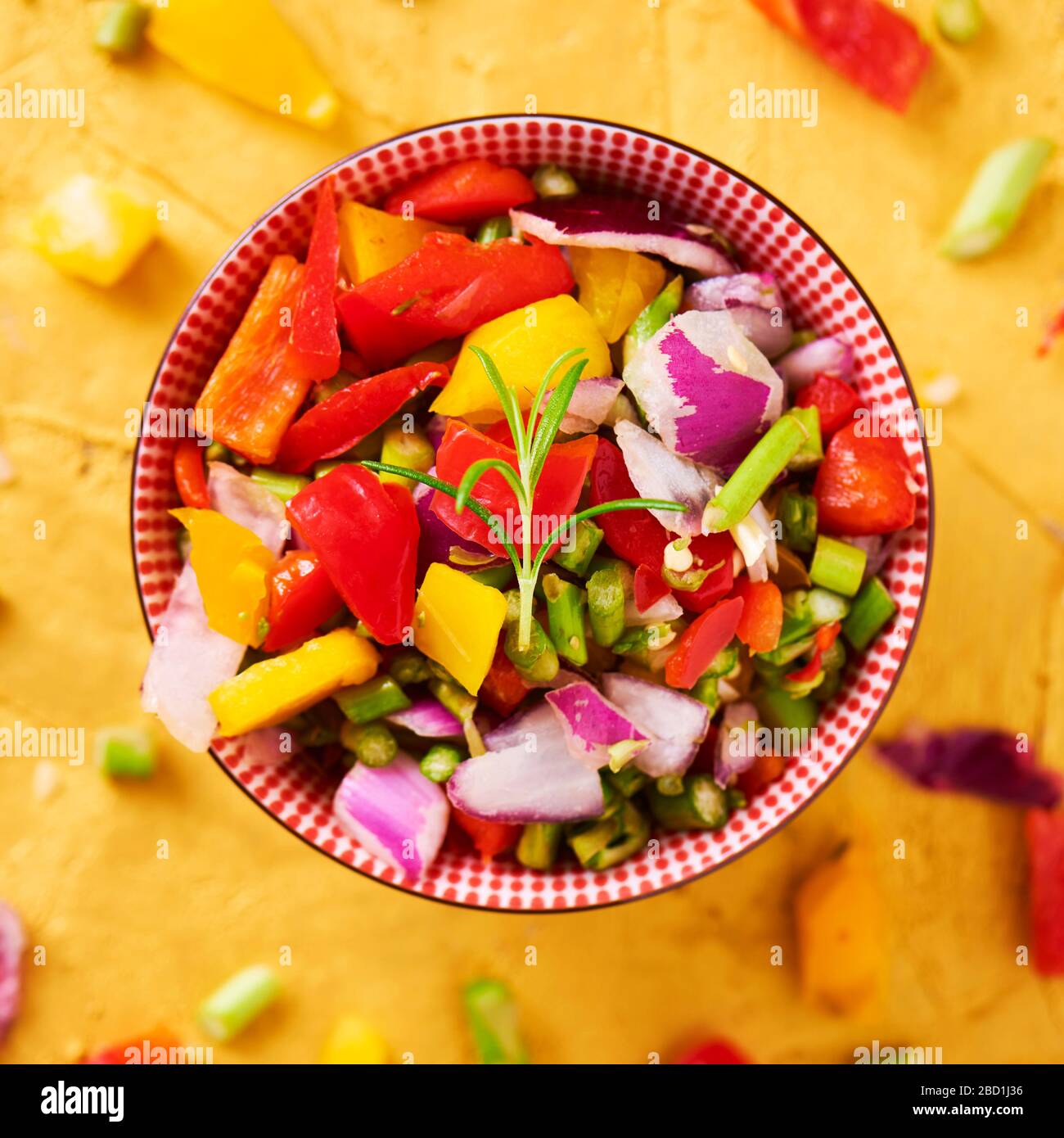 high angle view of a bowl with a mix of different raw chopped vegetables, such as asparagus, onion, or yellow and red bell pepper, on a golden texture Stock Photo