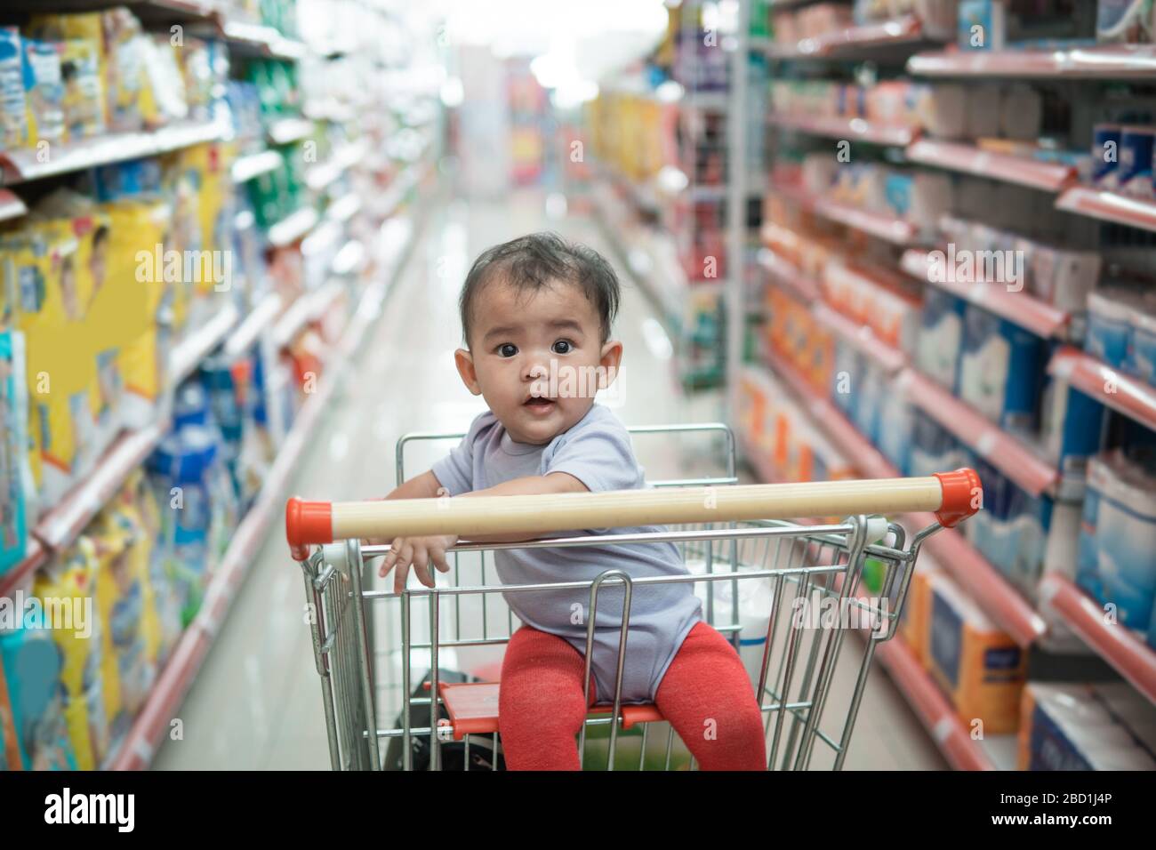 happy infant baby sitting alone in shopping cart or trolley in grocery