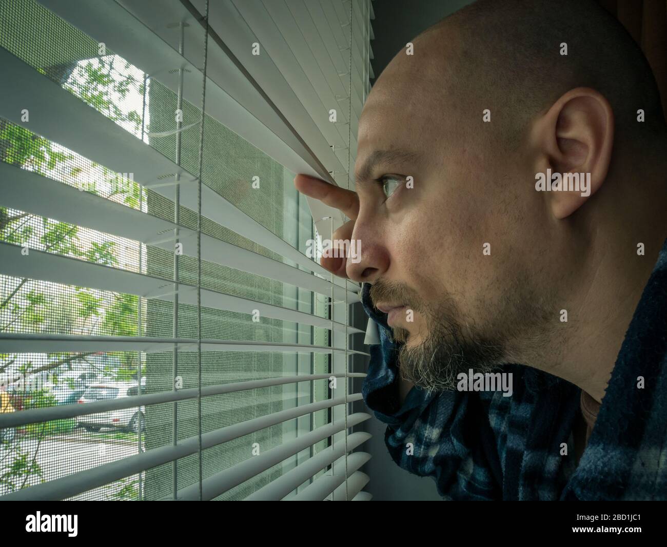Man in isolation looking through window blinds. Man forced to stay inside the house as a result of the restrictions caused by the Coronavirus outbreak Stock Photo