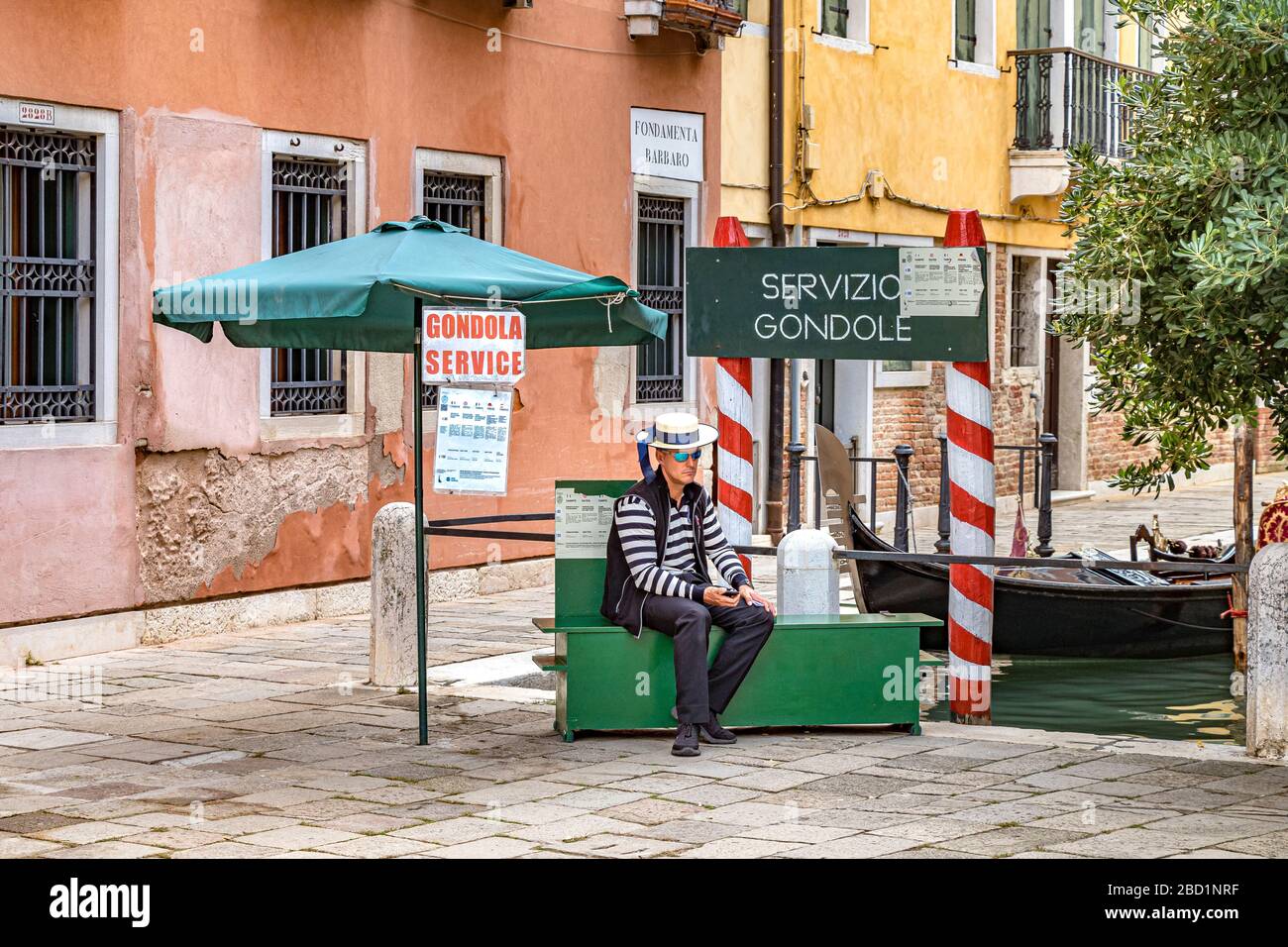 A Gondolier sitting down on a green box  waiting for tourists to take a gondola ride at Campo Santo Stefano ,Venice,Italy Stock Photo