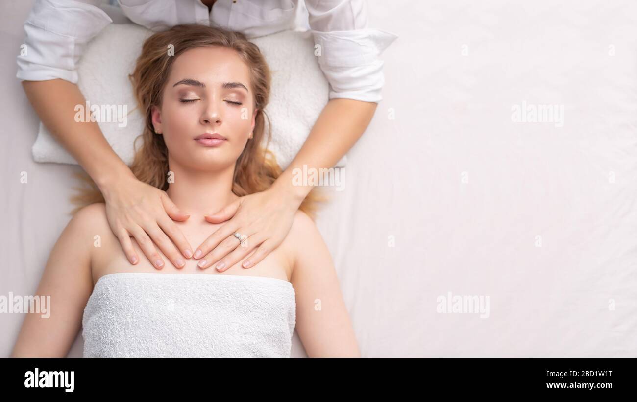 Female therapist healing a lying young girl by touch of her hands on a white background. Stock Photo