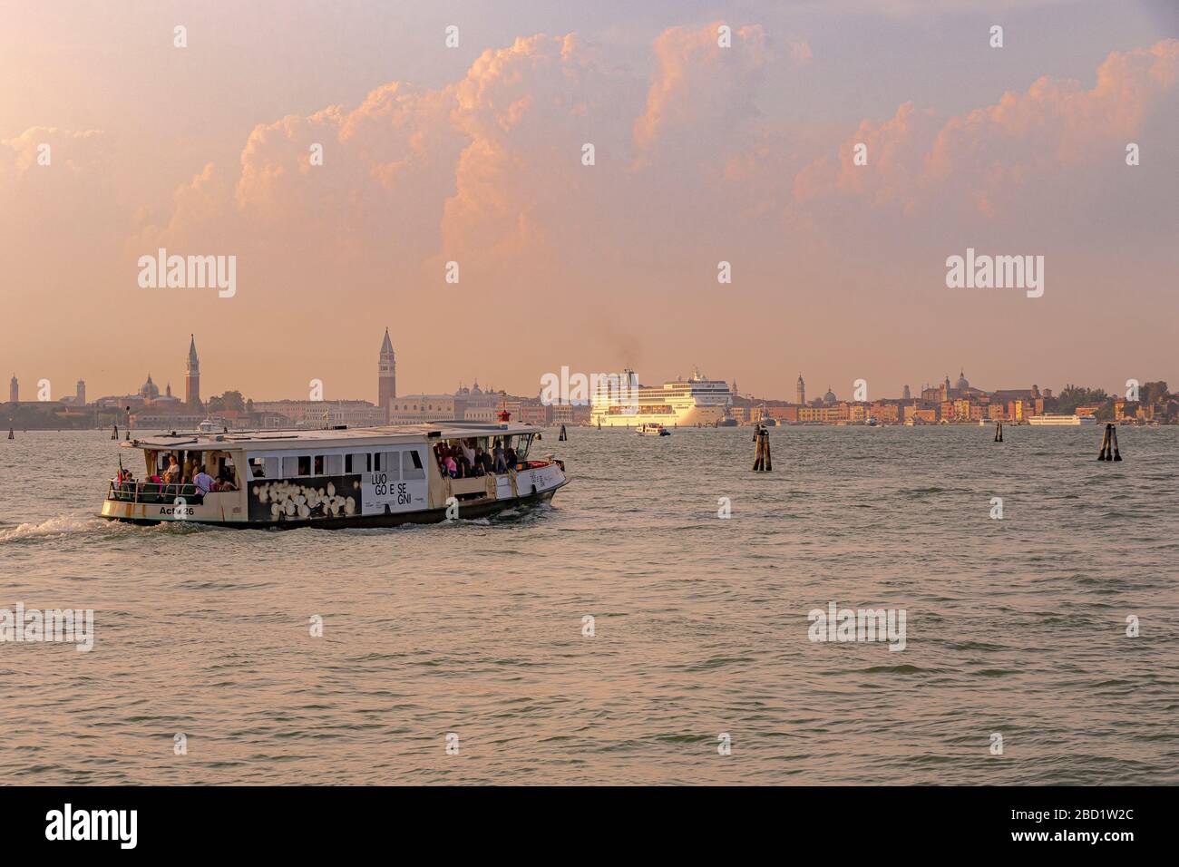 A Vaporetto leaving Lido towards Venice as a large cruise ship appears in the distance crossing the Venice lagoon ,Venice,Italy Stock Photo