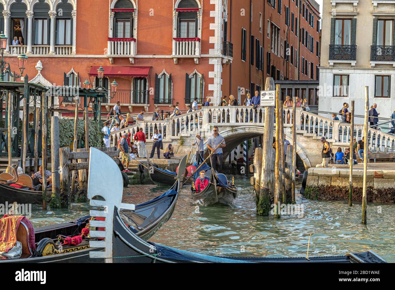 People standing on a canal bridge watching tourists taking gondola rides  in front of the Hotel Hotel Danieli on The Grand Canal ,Venice ,Italy Stock Photo